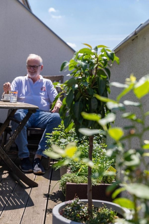 Sitzbereich auf einer begrünten Dachterrasse mit Tisch, Stuhl und Pflanzkübeln.